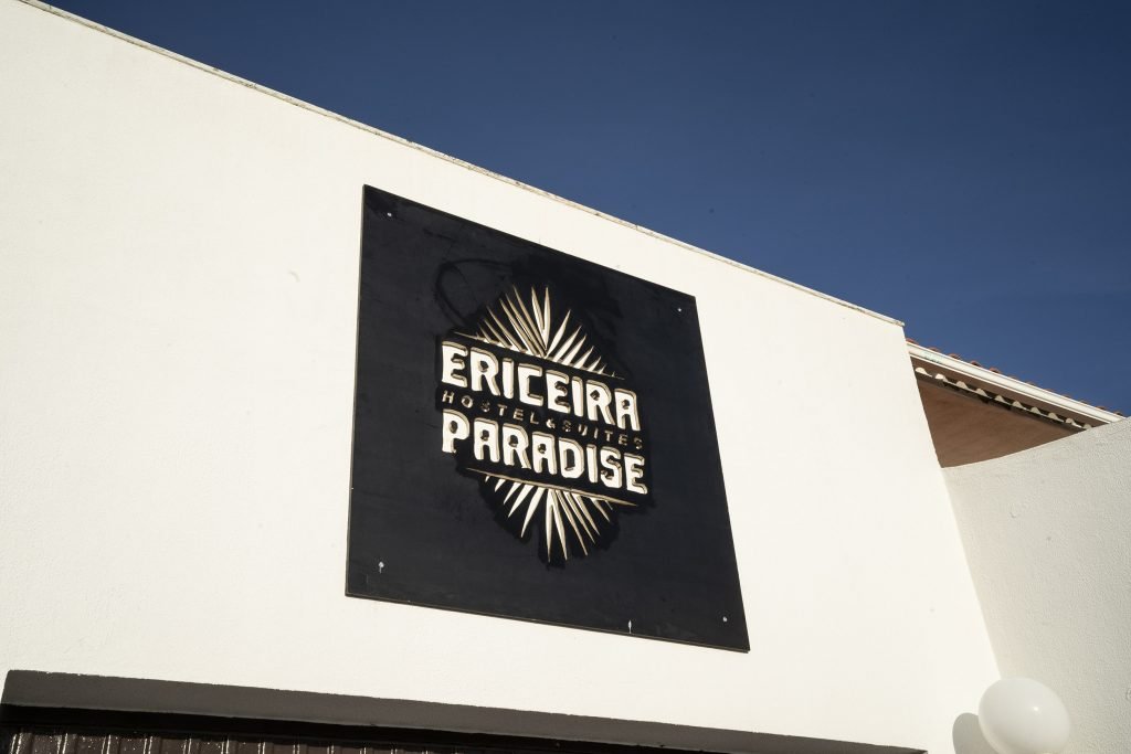 Sunny day with white walls and a black sign for Ericeira Paradise Guest House