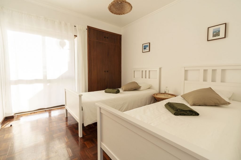 Twin bedroom with clean sheets and fresh towels, wooden accents and ocean photography in Portugal